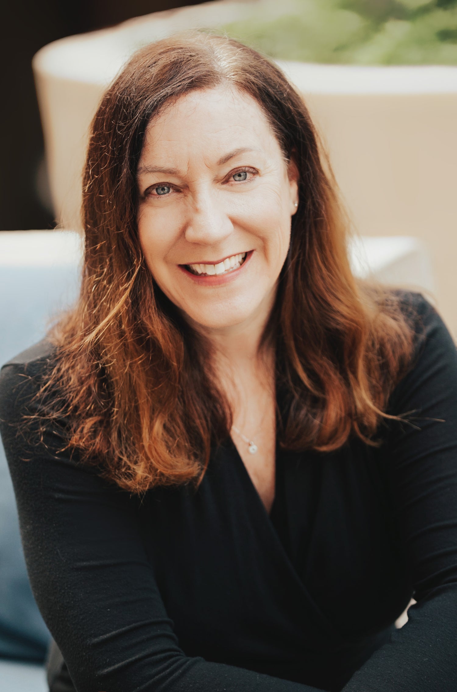 Woman with long brown hair wearing a black top, sitting outdoors.