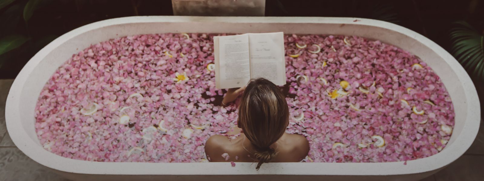 Person reading a book in a bathtub filled with pink flower petals